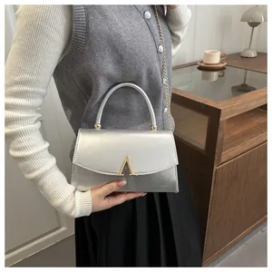 Détail d'un sac argenté métallisé avec fermoir en V doré et chaîne sur un mannequin