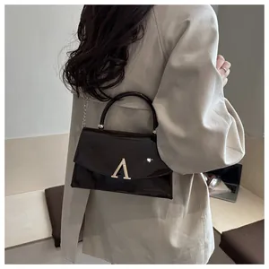 Détail du sac à bandoulière en cuir verni marron avec poignée dorée et logo chic