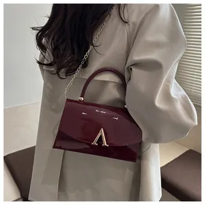 Détail d'un sac en cuir verni bordeaux avec boucle en V dorée et poignée ronde