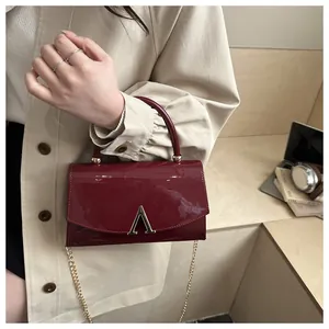 Détail du sac à main en cuir verni bordeaux avec chaîne dorée et logo métallique