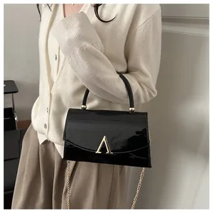 Détail du sac en cuir verni noir avec boucle dorée en A et bandoulière chaîne