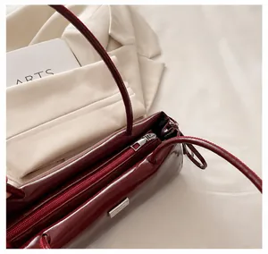 Detail view of smooth metal zipper on burgundy glossy faux leather baguette bag