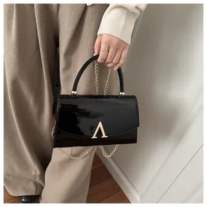 Détail de sac à main en cuir verni noir brillant avec boucle dorée et bandoulière chaîne