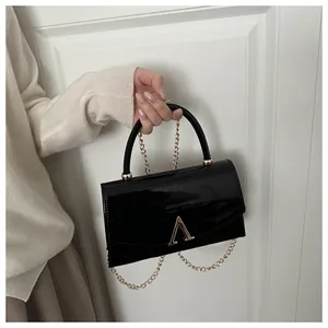 Détail d'un sac à main en cuir verni noir brillant avec boucle en V dorée et chaîne