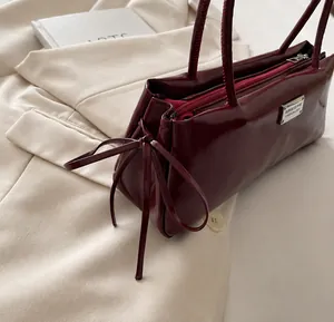 Close-up of a burgundy patent leather tote bag featuring a decorative side bow detail