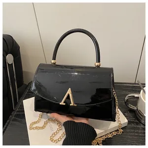 Détail macro du sac en cuir verni noir brillant avec un fermoir doré en forme d'A