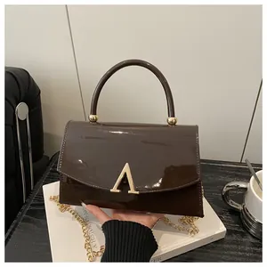 Détail d'un sac à main en cuir verni marron chocolat avec boucle dorée en A et chaîne