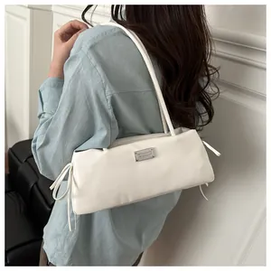 Detail of white baguette shoulder bag featuring silver metal plaque and side drawstring