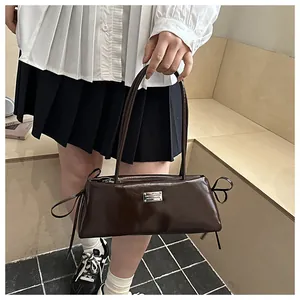 Detail of dark brown glossy patent leather baguette bag with side bow accents and metal logo