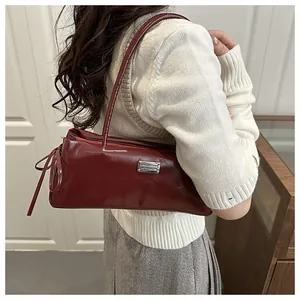 Detail of dark red glossy faux leather underarm bag with silver metal logo plaque