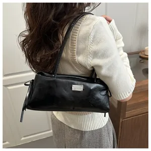 Close-up of black glossy baguette bag worn on shoulder, showing shiny leather and silver metal tag