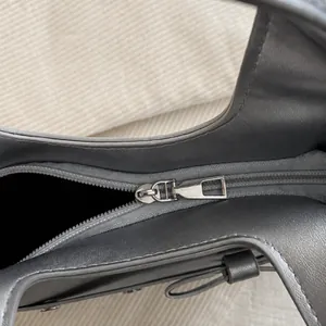 Makro-Detail des silbernen Metallreißverschlusses und der grauen PU-Lederstruktur der Tasche