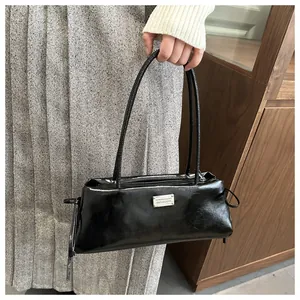 Detail of glossy black faux leather baguette bag with silver metallic plaque on side