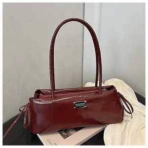 Detail of burgundy patent leather shoulder bag with silver plaque and side tie accents