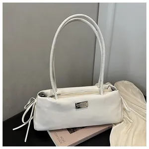 Detail of creamy white faux leather baguette bag with silver plate and side ribbon bows