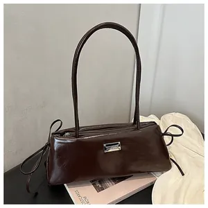 Detail of dark brown leather baguette bag with silver plaque on a decorative book