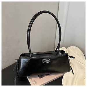 Detailed macro view of the silver metal plaque on a glossy black patent leather baguette bag