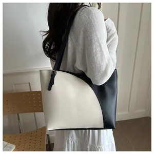 Side view of a contrast color tote bag with asymmetric black and white leather stitching