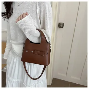 Detail of dark brown leather shoulder bag with decorative bow and silver eyelets