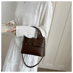 Detail of dark brown leather shoulder bag with bow decoration and metal eyelet straps