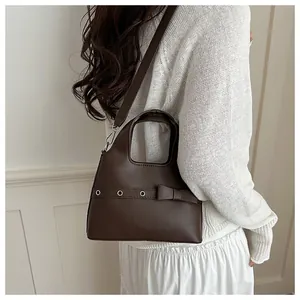 Detail view of brown leather bucket bag featuring decorative bow and metal eyelets on model