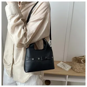 Detailed view of a black leather bucket bag with ribbon and metal eyelets on a model