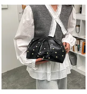 Detalle de bolso de mano negro con textura de cocodrilo, tachuelas doradas y pliegues