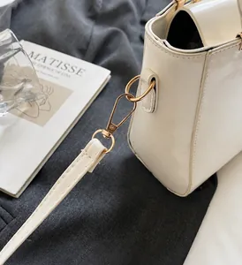 Detail of glossy off-white handbag featuring shiny gold metal hardware and hook attachment