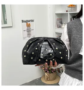Detalle del bolso de mano negro con grabado de cocodrilo, tachuelas doradas y diseño plisado