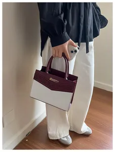Detail of the chic burgundy and beige color-block handbag with gold metallic logo
