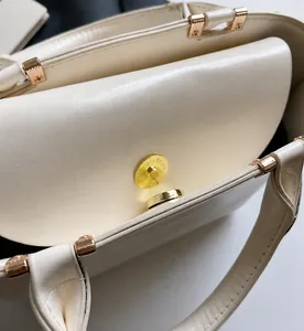 Close-up of golden magnetic buckle and smooth cream leather texture on handbags