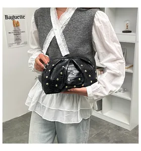 Detalle de bolso de mano de piel de cocodrilo negra con tachuelas doradas y pliegues