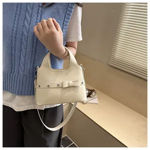 Detail of cream soft leather bucket bag with bow accent and metallic eyelet hardware