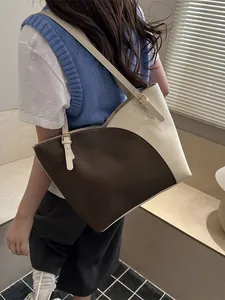 Large color-block tote bag in brown and cream leather worn by a model in a minimal setting