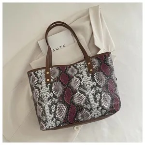 Détail du sac cabas motif serpent violet avec rivets dorés sur un blazer blanc