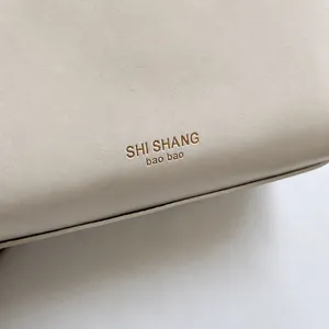 Detail view of cream leather square bag texture with gold logo branding on front