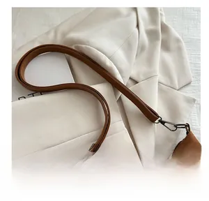Detail of brown faux suede crossbody bag featuring black metal hook and thin shoulder strap