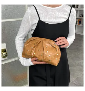 Detalle de bolso de mano plisado marrón con tachuelas doradas sostenido por una modelo