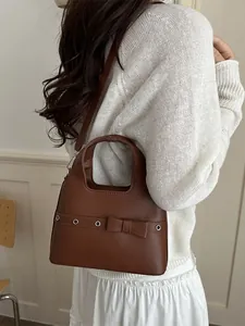 Brown soft leather hobo bag with bow and metal eyelets shown on model
