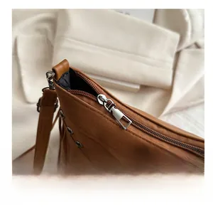 Close-up of smooth metal zipper and long fringe details on brown suede crossbody bag
