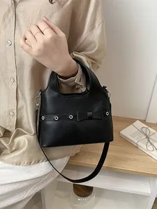 Minimalist black faux leather tote bag with bow detail and adjustable shoulder strap
