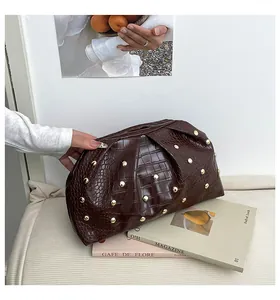 Detalle del bolso de mano marrón oscuro efecto cocodrilo con tachuelas doradas redondas