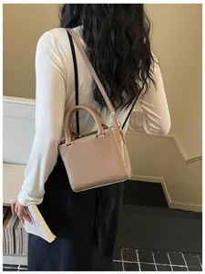 Brown faux leather square tote bag shown on shoulder with adjustable strap and top handles