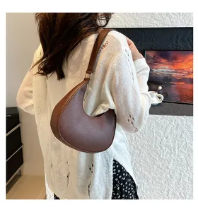 Brown lychee leather crescent bag shown on shoulder in a cozy indoor setting