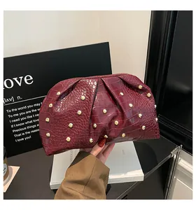 Detalle de bolso burdeos con grabado de cocodrilo, remaches dorados y pliegues