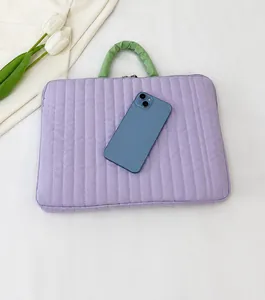 Detail of purple quilted laptop sleeve with sage green handle on a bed background