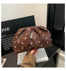 Detalle de un bolso de mano marrón plisado con textura de cocodrilo y remaches dorados