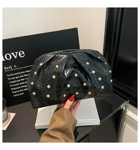 Detalle de cuero negro con patrón de cocodrilo y tachuelas doradas en bolso fruncido