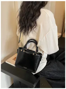 Glossy black square handbag featuring golden hardware and a cylindrical top handle