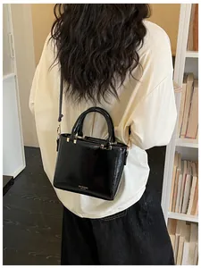 Detail of black patent leather crossbody bag with gold hardware and logo on model